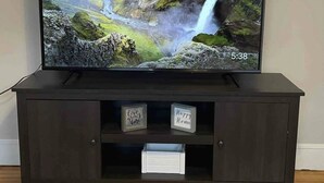 A flat-screen TV on a dark wooden TV stand with two framed signs saying "Love grows here" and "Happy Home."