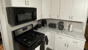 A compact kitchen with white cabinets, a black microwave, a stove, and a coffee maker.