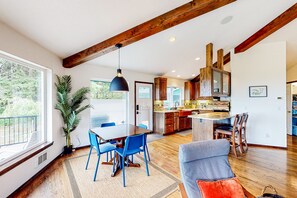 A spacious living area with a dining table, blue chairs, a grey sofa, and wooden flooring. - Idyllic home with water views, wrap-around deck, hot tub, and firepit - dogs ok (Port Angeles)