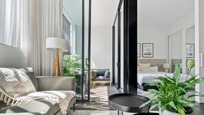 Une chambre d’hôtel moderne avec un canapé, une petite table, une plante en pot et un lit doté d’une tête de lit.