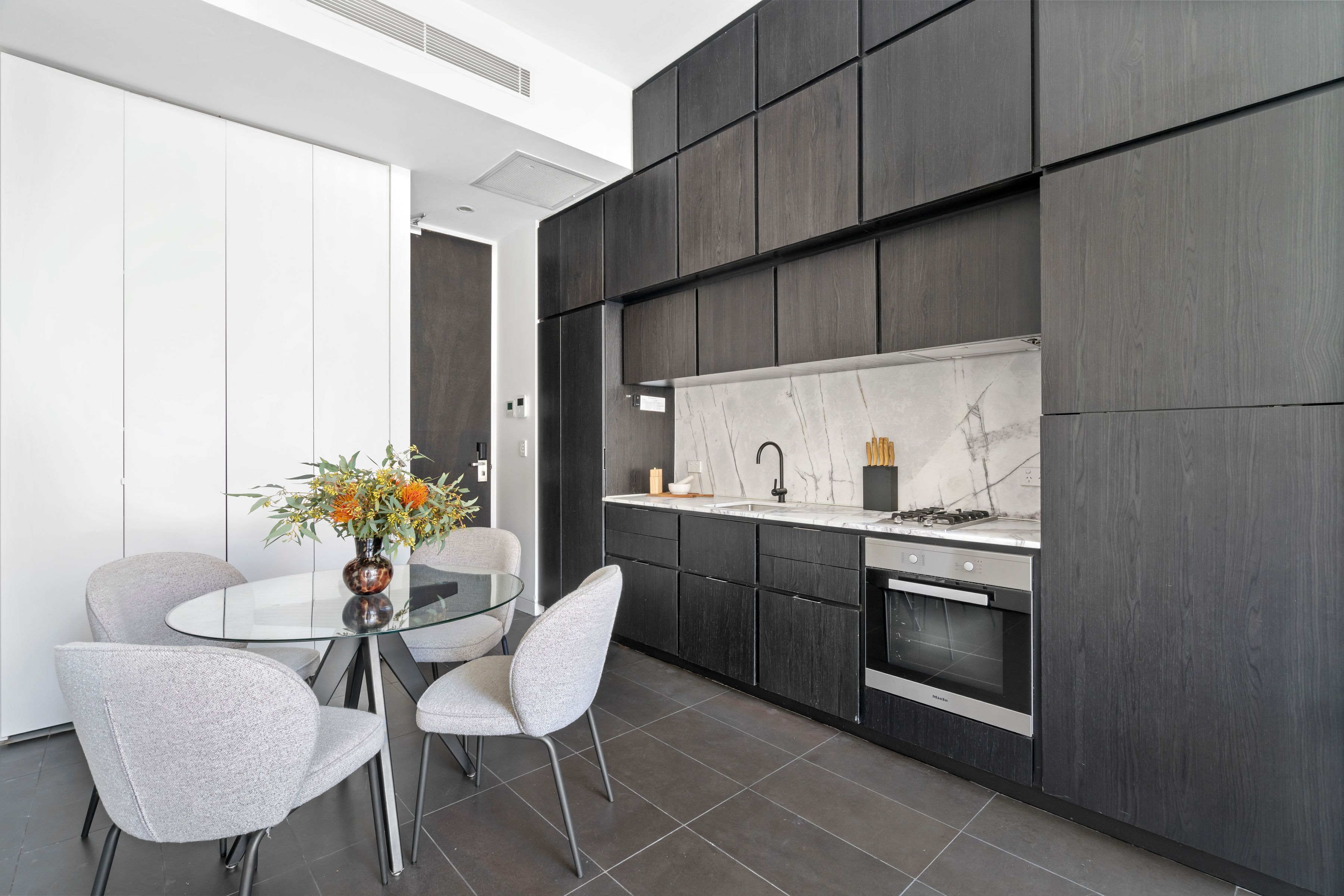 Una cocina moderna con una isla central, armarios de madera oscura y encimera blanca.