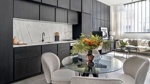 Une cuisine moderne avec des meubles de couleur sombre, un plan de travail en marbre et une table à manger en verre, accompagnée de chaises.