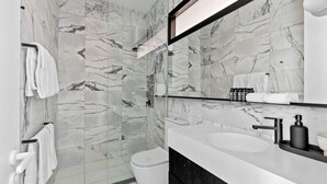 Une salle de bain moderne avec des murs en marbre, un lavabo blanc et un meuble-lavabo noir.