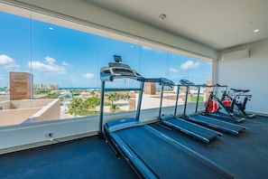A gym with treadmills and stationary bikes, large windows with a city view, and a modern interior design.