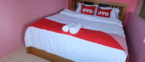 Una cama bien hecha con ropa de cama blanca y roja, dos almohadas con el texto 'OYO' y dos toallas enrolladas.
