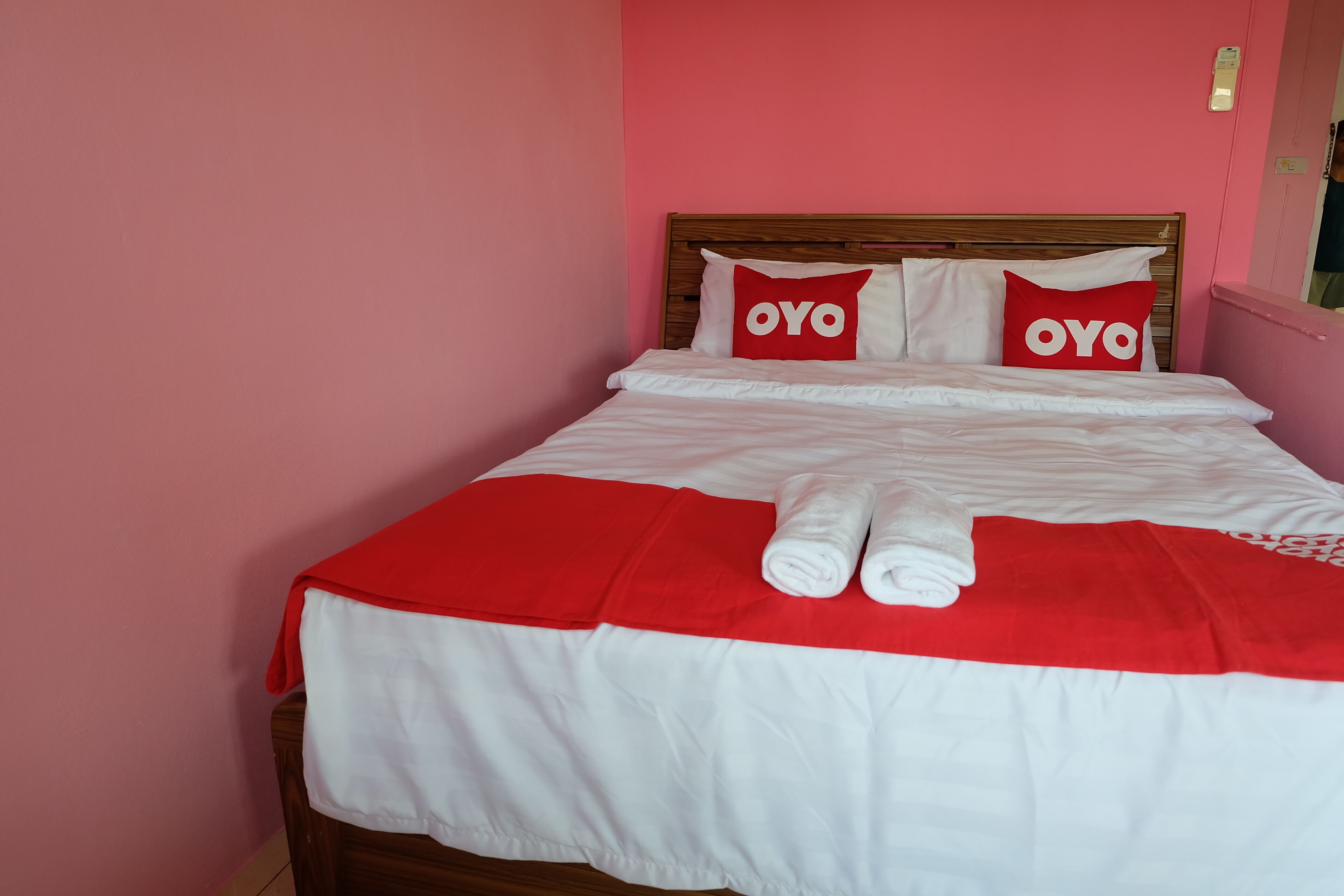 Una cama con una colcha roja y blanca, dos almohadas con la palabra 'OYO' y dos toallas enrolladas sobre la cama.