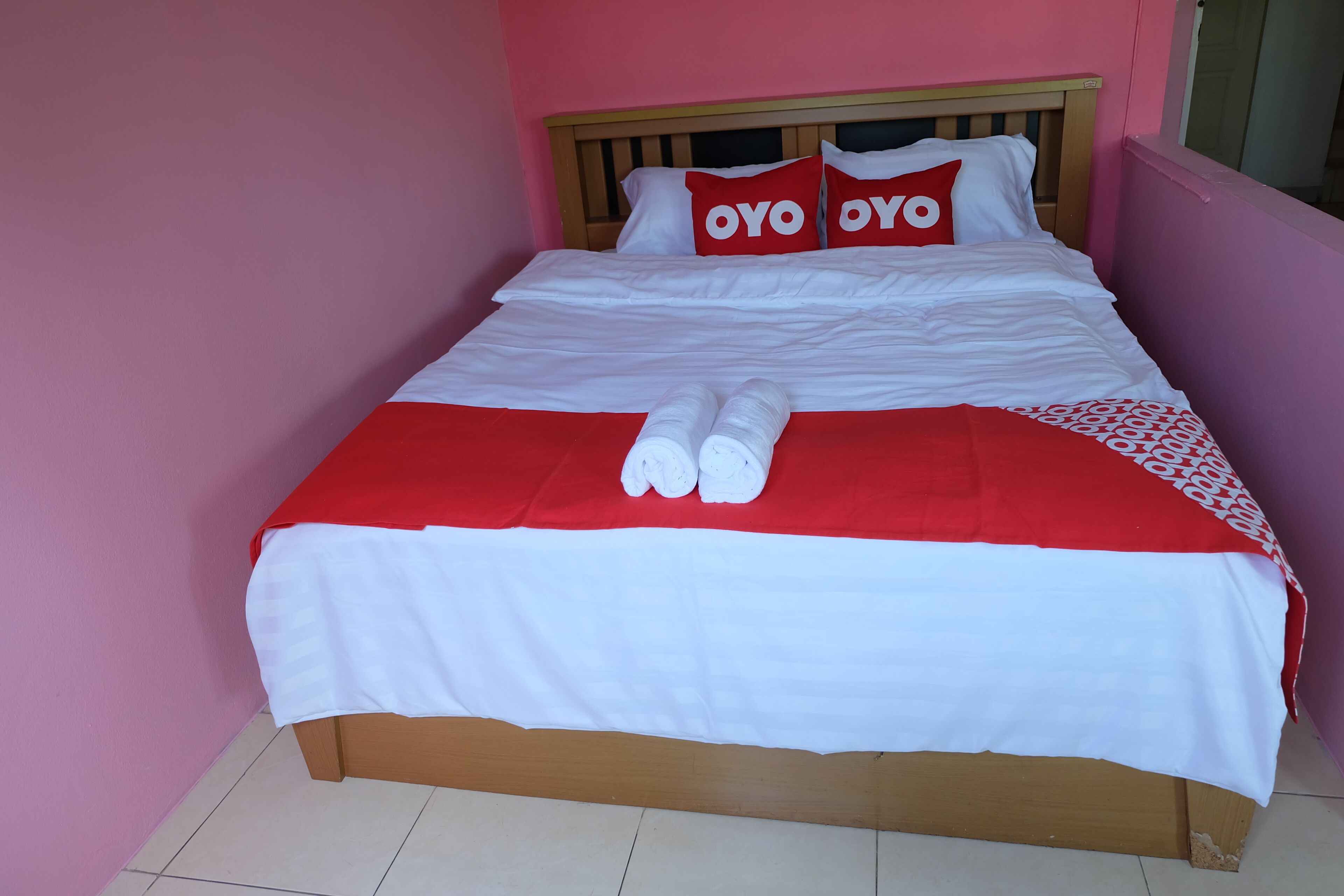 A bed with a wooden headboard, white and red bedding, and two pillows with the word "OYO" on them.