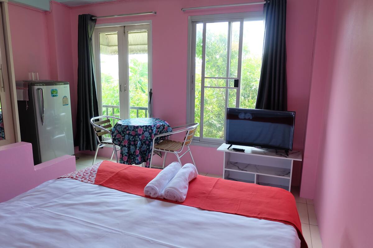 A room with a bed, a table with chairs, a TV, and a refrigerator.