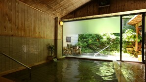A traditional wooden interior with a stone-tiled floor, a wooden bench, and a glass door leading to an outdoor garden. - Nukumorino-yado Komanoyu (Kiso)