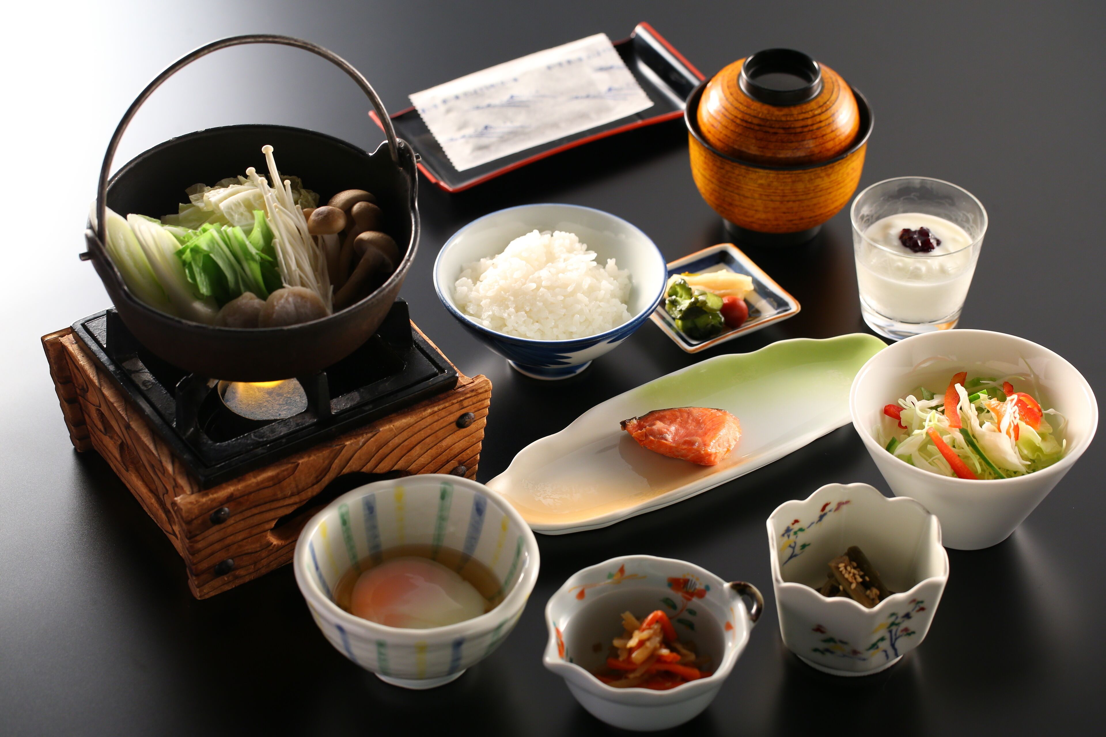 Una comida tradicional japonesa con un recipiente de comida hirviendo, tazones de arroz y diferentes acompañamientos.