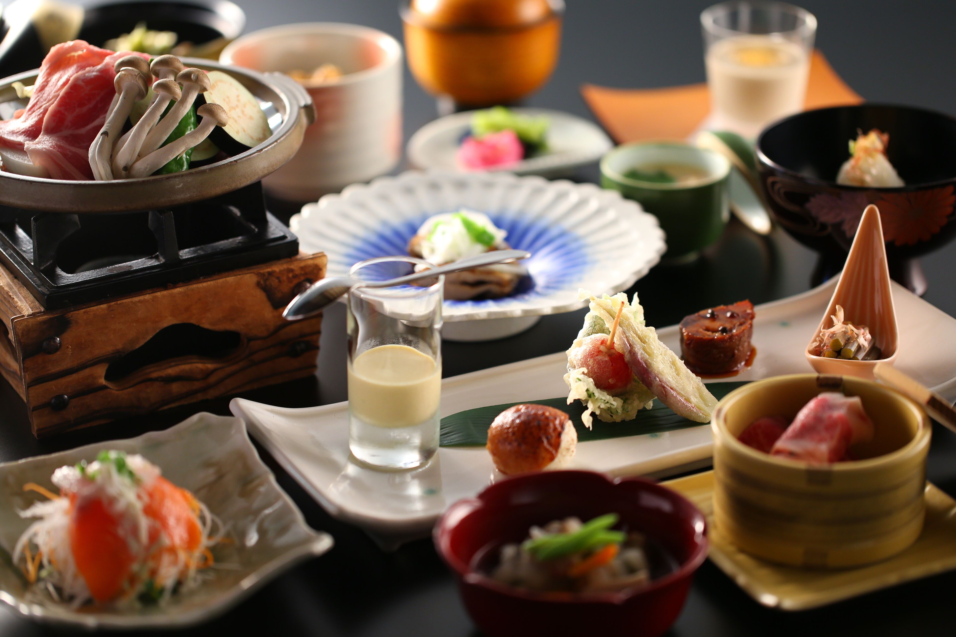 A variety of Japanese dishes on a table, including sushi, sashimi, and a hot pot.
