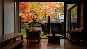 A room with a wooden floor, two sofas, a bench, and a table with a vase. - Nukumorino-yado Komanoyu (Kiso)