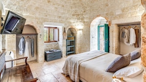 A stone-walled bedroom with a bed, a wardrobe, a desk, and a television mounted on the wall. - Trullo La Sacchina in Ostuni (Ostuni)