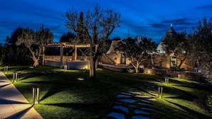 A stone building with a conical roof, a pergola with string lights, and a pathway leading to a gazebo. - Trullo La Sacchina in Ostuni (Ostuni)