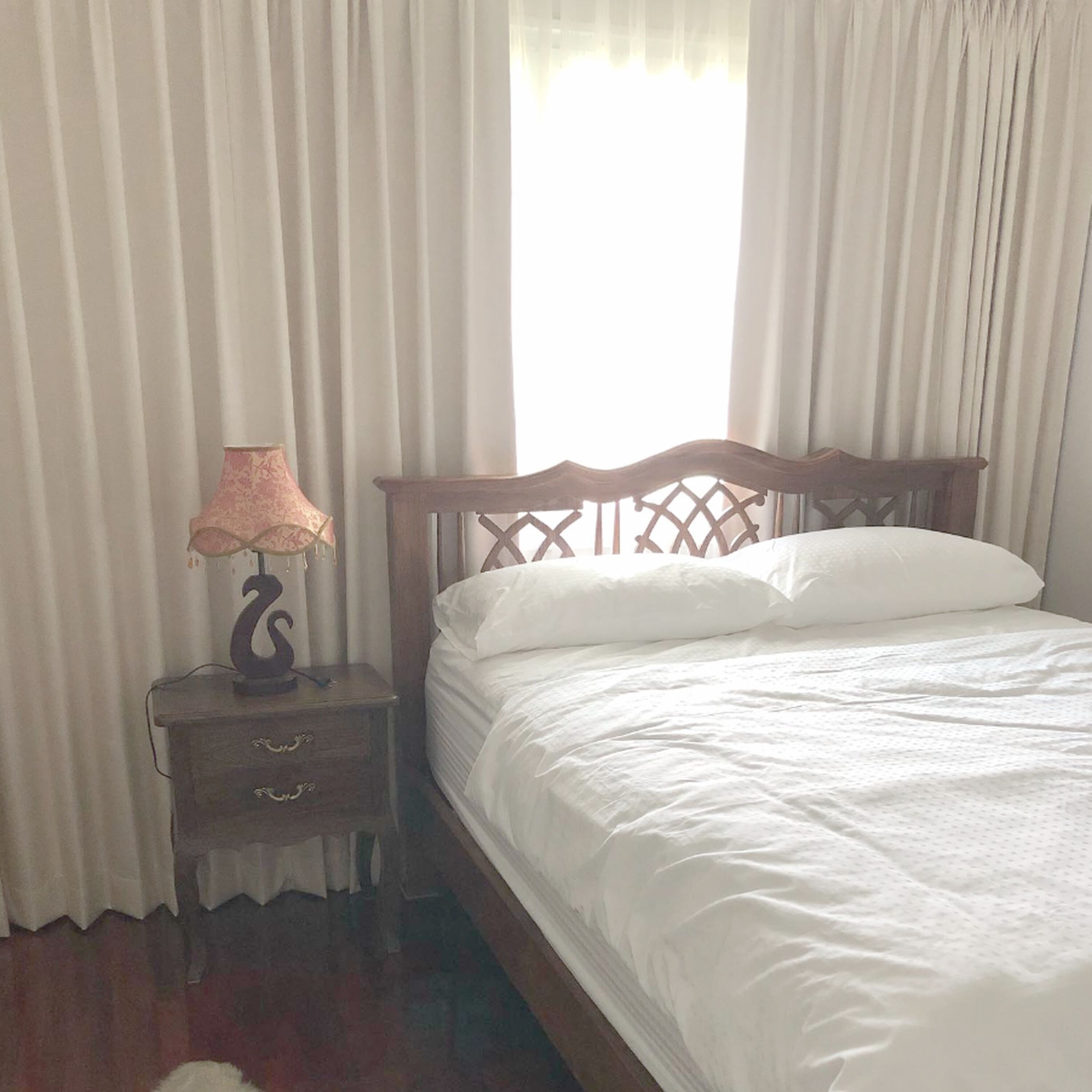 A neatly made bed with white linens in a room with wooden headboard and a nightstand with a lamp.