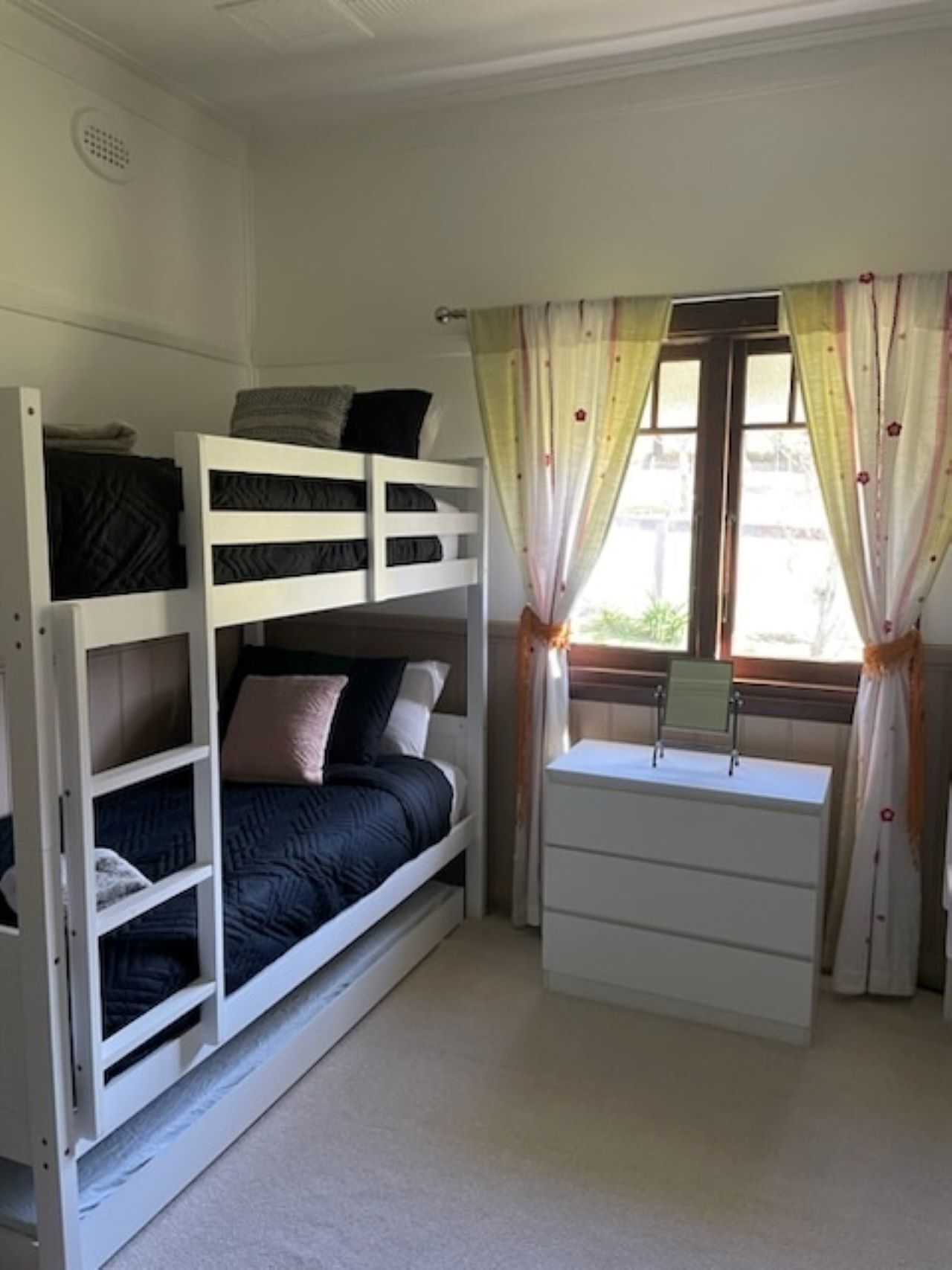 A bunk bed with a desk and drawers, a window with curtains, and a radiator.