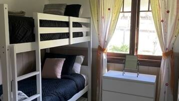 A bunk bed with a desk and drawers, a window with curtains, and a radiator.