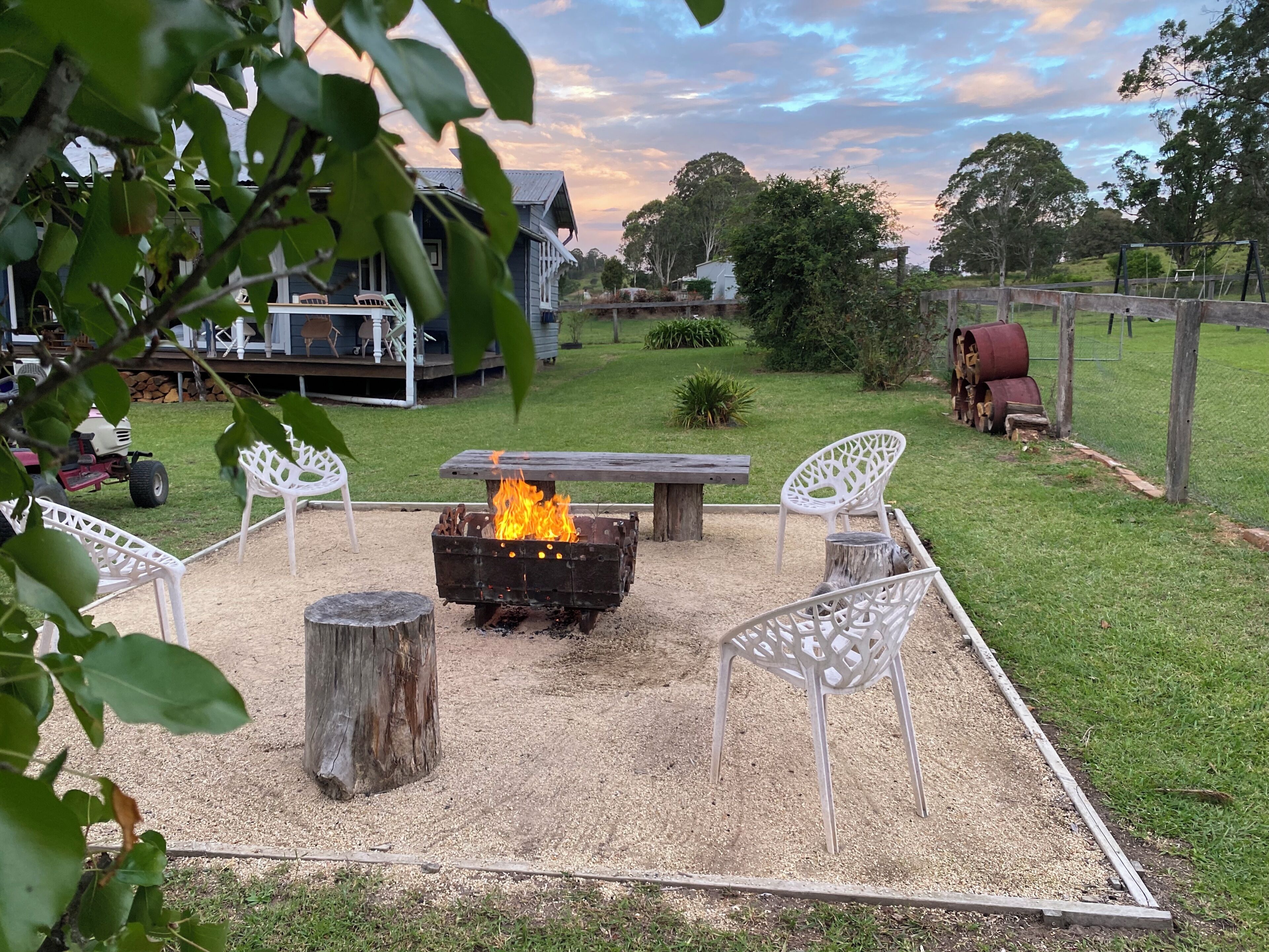 Un jardin avec un foyer, des chaises blanches et une table en bois.