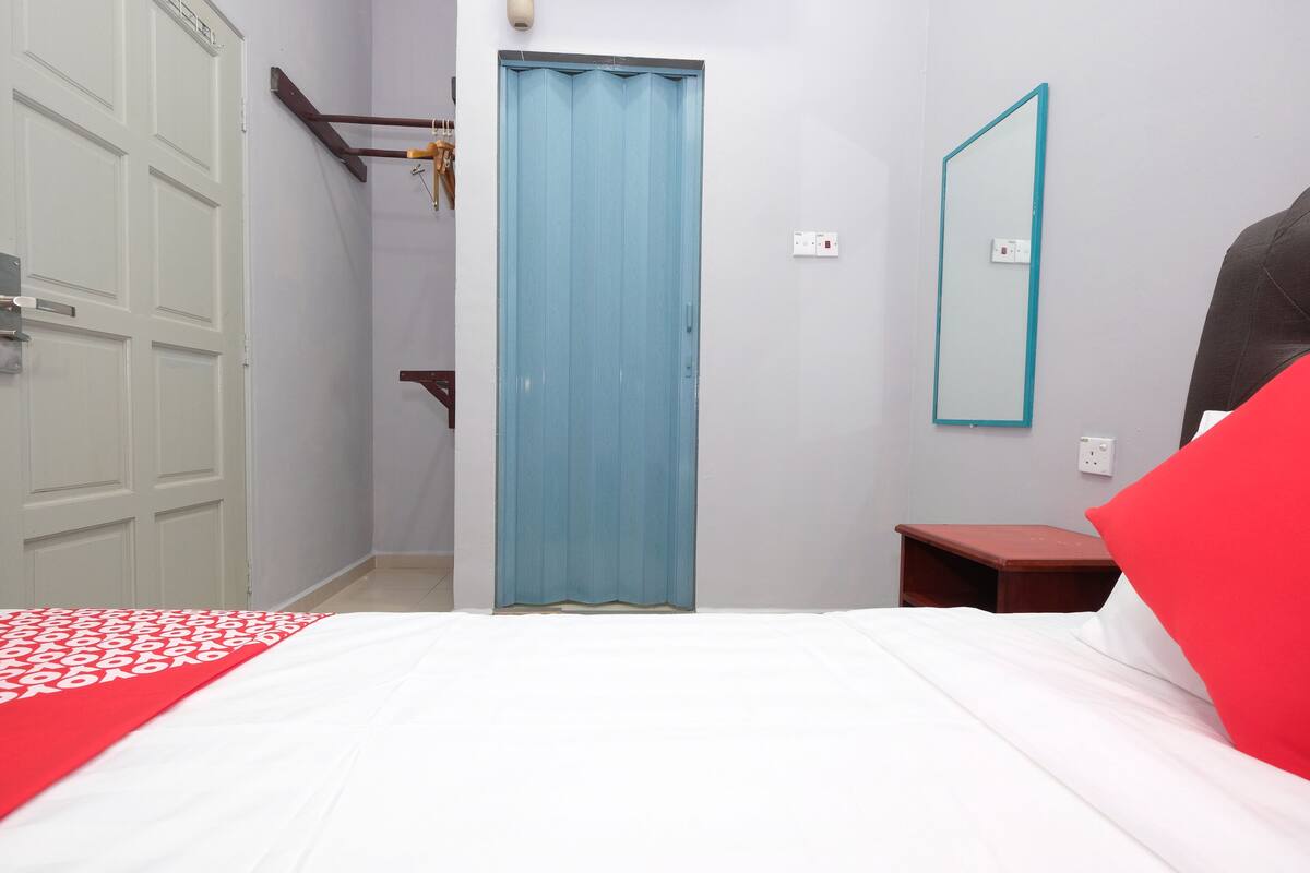 A bedroom with a bed, a blue door, a mirror, and a small wooden table.