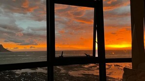 A room with a large window overlooking a beach at sunset. - Oppulent Apartment on the Beach (Cape Town)