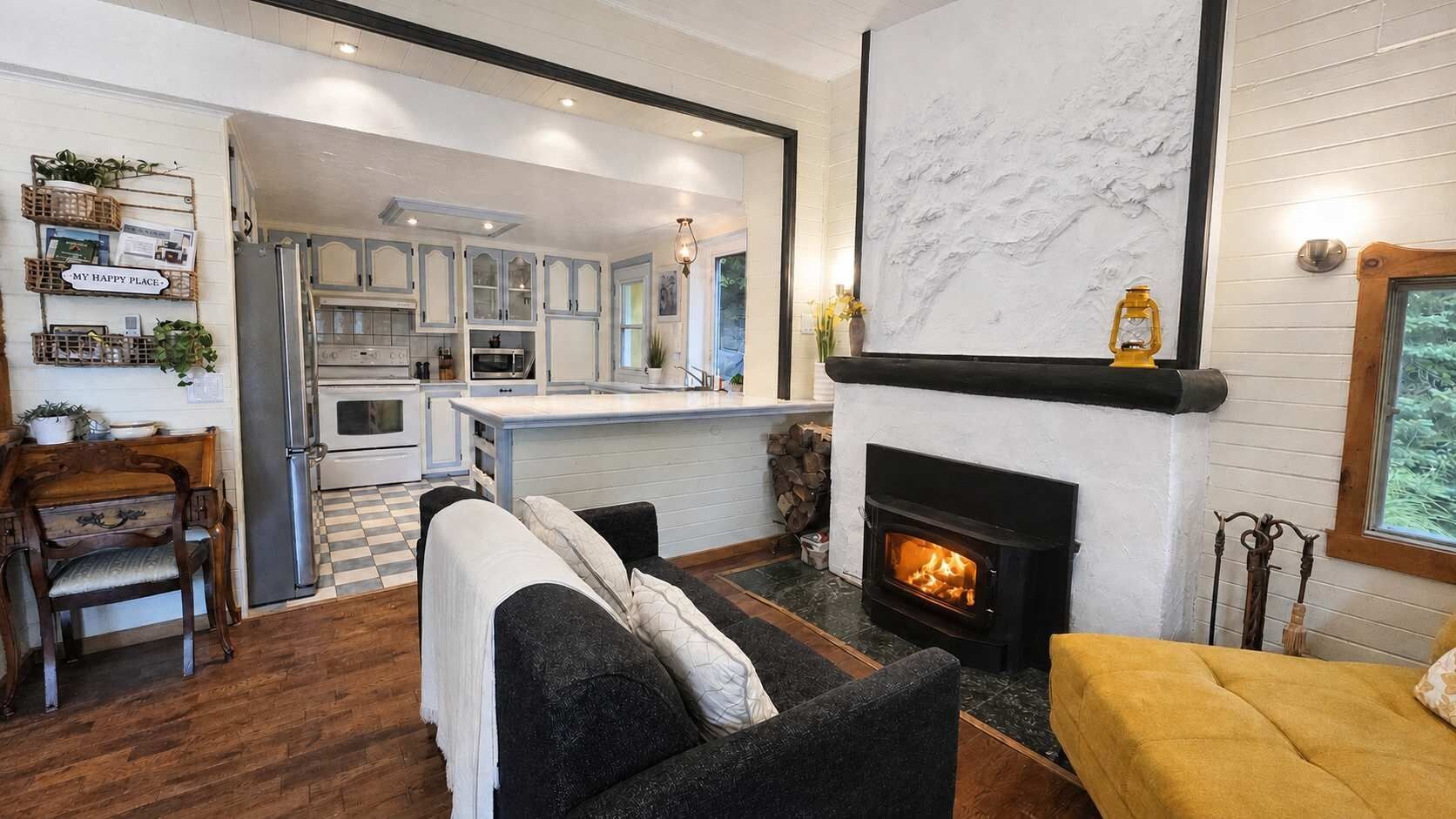 A cozy living room with a fireplace, a sofa, and a dining area with a kitchen in the background.