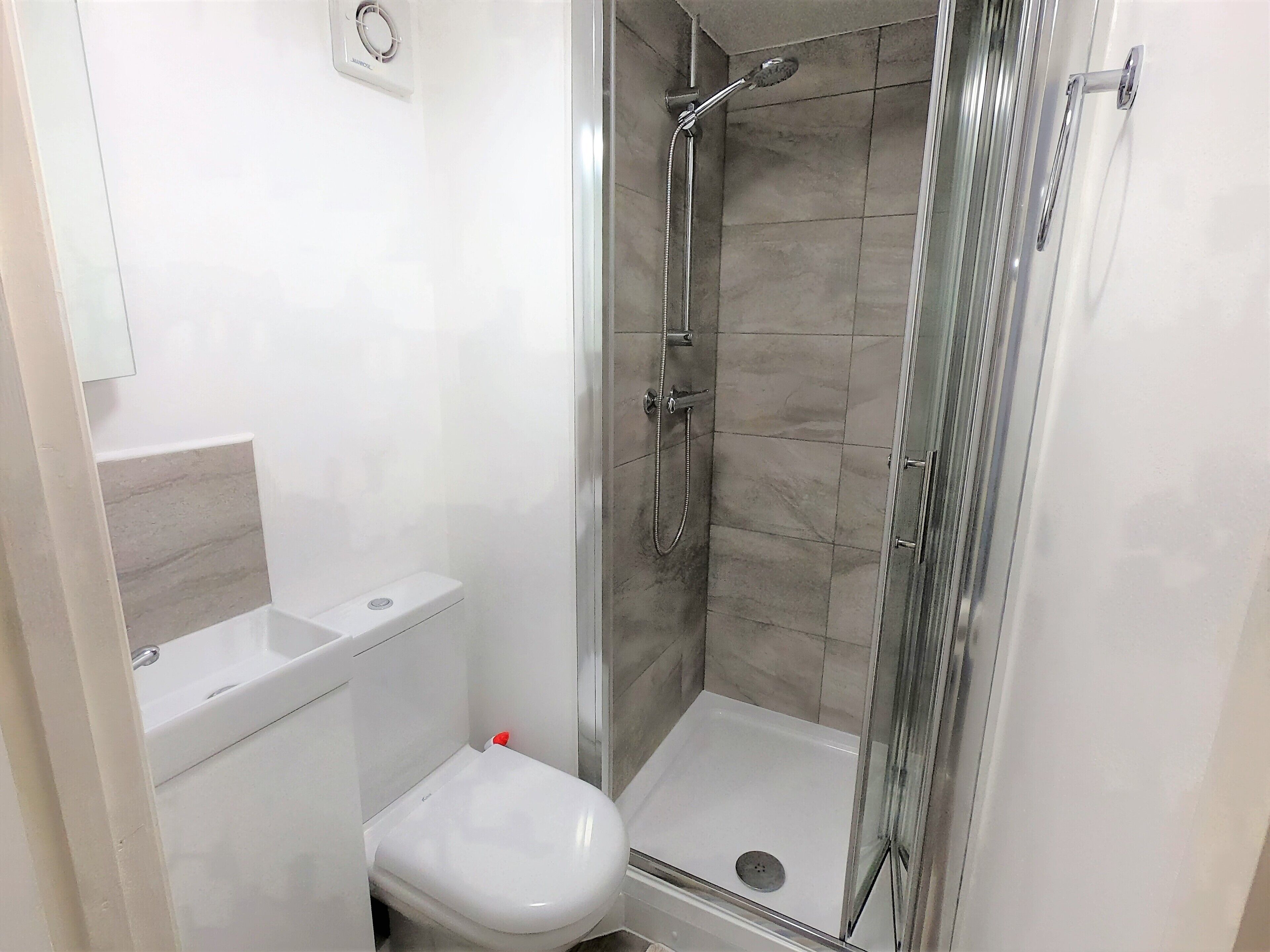 A bathroom with a glass-enclosed shower, a white toilet, and a marble-tiled shower wall.