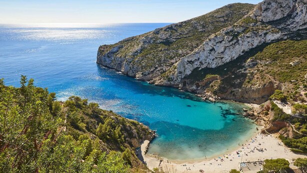 Un paisaje costero con una playa, acantilados rocosos y aguas azules cristalinas.