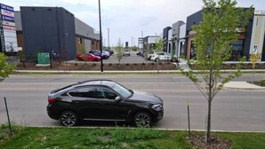 A black car parked on a street with a sidewalk and a small tree in the foreground. - Creekwood Luxury 1 Bed Lower Level Suite (Edmonton)