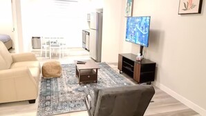 A living room with a sofa, a coffee table, a rug, a TV, and a wall-mounted TV. - Creekwood Luxury 1 Bed Lower Level Suite (Edmonton)