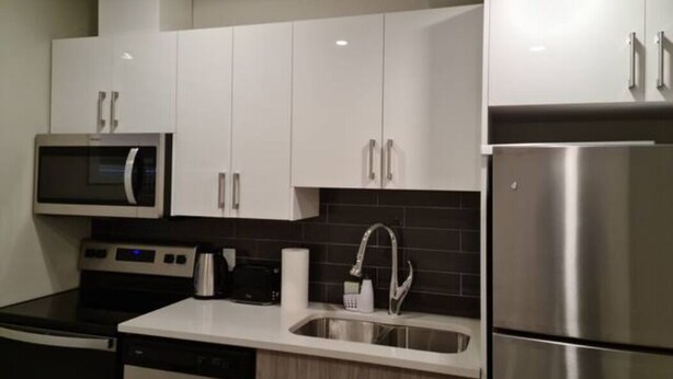 A modern kitchen with white cabinets, stainless steel appliances, and a black countertop. - Creekwood Luxury 1 Bed Lower Level Suite (Edmonton)