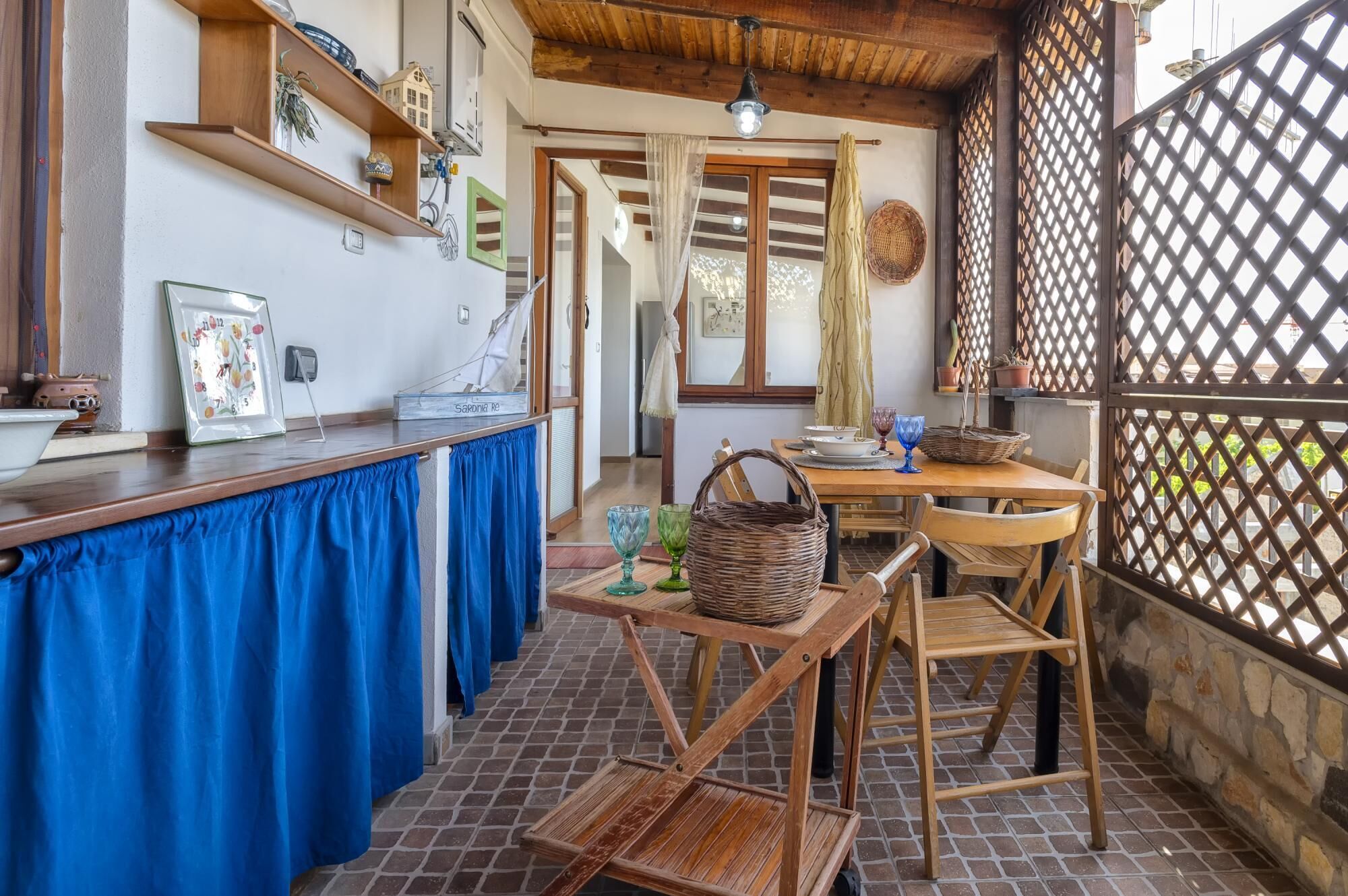 Une cuisine rustique, avec des meubles en bois, un sol carrelé et une vue sur l’extérieur à travers une porte à treillis.