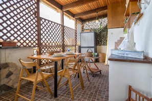A covered outdoor dining area with wooden tables and chairs, a whiteboard, and a rustic wooden shelf with a decorative item.