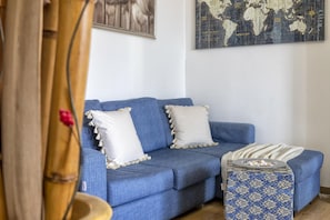 A blue sofa with white pillows and a patterned ottoman in a room with a world map on the wall.