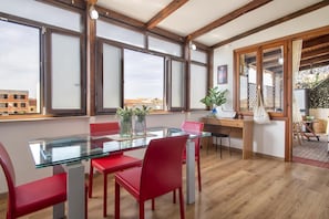 A modern dining area with a glass table, red chairs, and wooden beams.