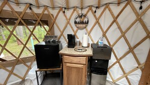 Una kitchenette compacta con cafetera, dispensador de agua y un cubo de basura dentro de una estructura tipo tienda de campaña.