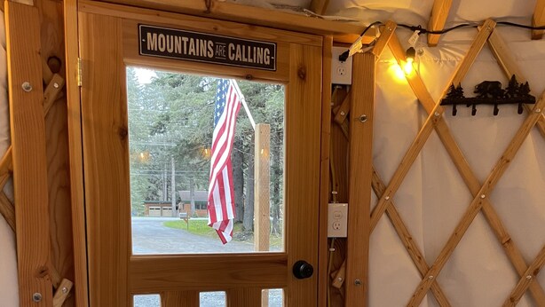 Una puerta de madera con un letrero que dice 'Mountains are calling'. Una bandera estadounidense cuelga de la puerta.