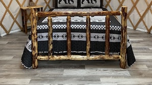 Interior acogedor de una yurta con una cama que presenta un edredón estampado y dos almohadas con diseños de osos, una pequeña mesa de madera y un letrero en la pared que dice 'Adventure Awaits'.