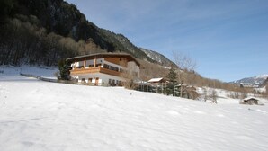 Una amplia cabaña de dos plantas con balcón, rodeada de colinas y montañas nevadas.