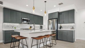 A modern kitchen with grey cabinets, stainless steel appliances, and a central island with bar stools.