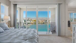 A bedroom with a large bed, a view of a swimming pool, and a balcony with chairs.