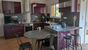 Moderni keittiö, jossa on tummanvioletit kaapit, keskellä oleva saareke jakkaroineen, sisäänrakennettu uuni ja suuri ikkuna, josta tulee runsaasti luonnonvaloa.