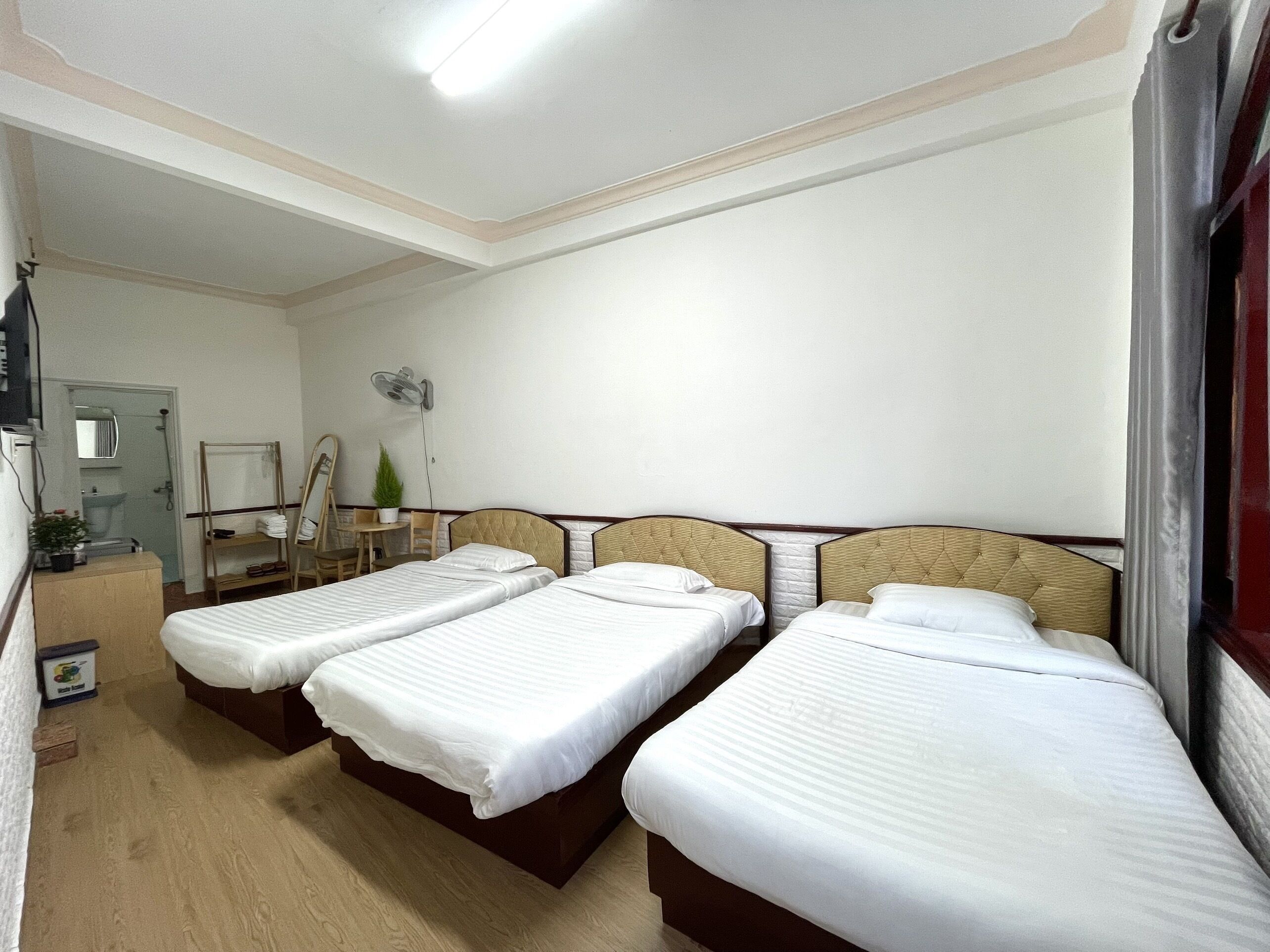 A hotel room with three single beds, a small desk, a chair, a mirror, and a fan.