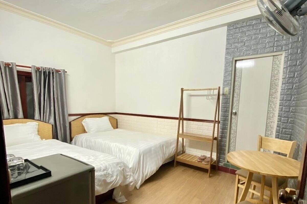 A hotel room with two single beds, a small table with chairs, a desk, and a mirror.