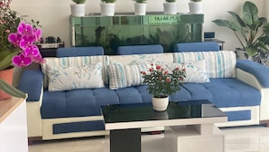 Un salon moderne avec un canapé bleu, une table basse en verre et plusieurs plantes en pot.