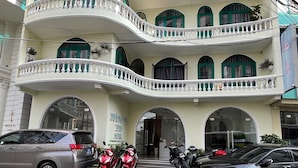 Un hôtel à plusieurs étages, doté d’une façade incurvée, de balcons avec des garde-corps blancs et de fenêtres en arc de cercle.