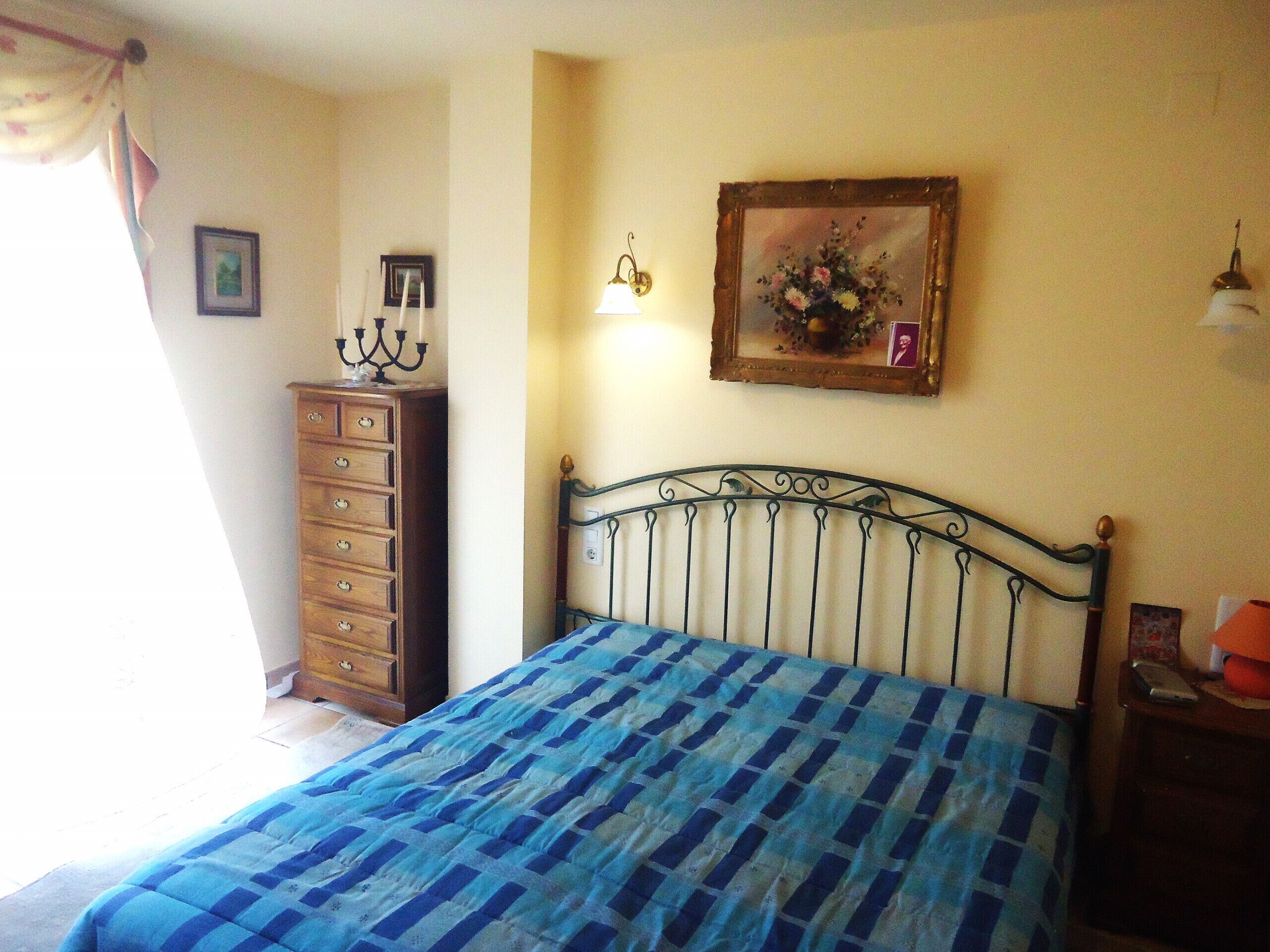 A bedroom with a bed, dresser, and wall-mounted lamp.