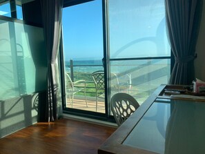 A room with a large window offering a view of the ocean and a balcony with chairs. - Happiness Inn (Hengchun)
