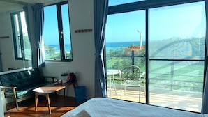 A hotel room with a bed, a sofa, a table, and a balcony with a view of the ocean. - Happiness Inn (Hengchun)