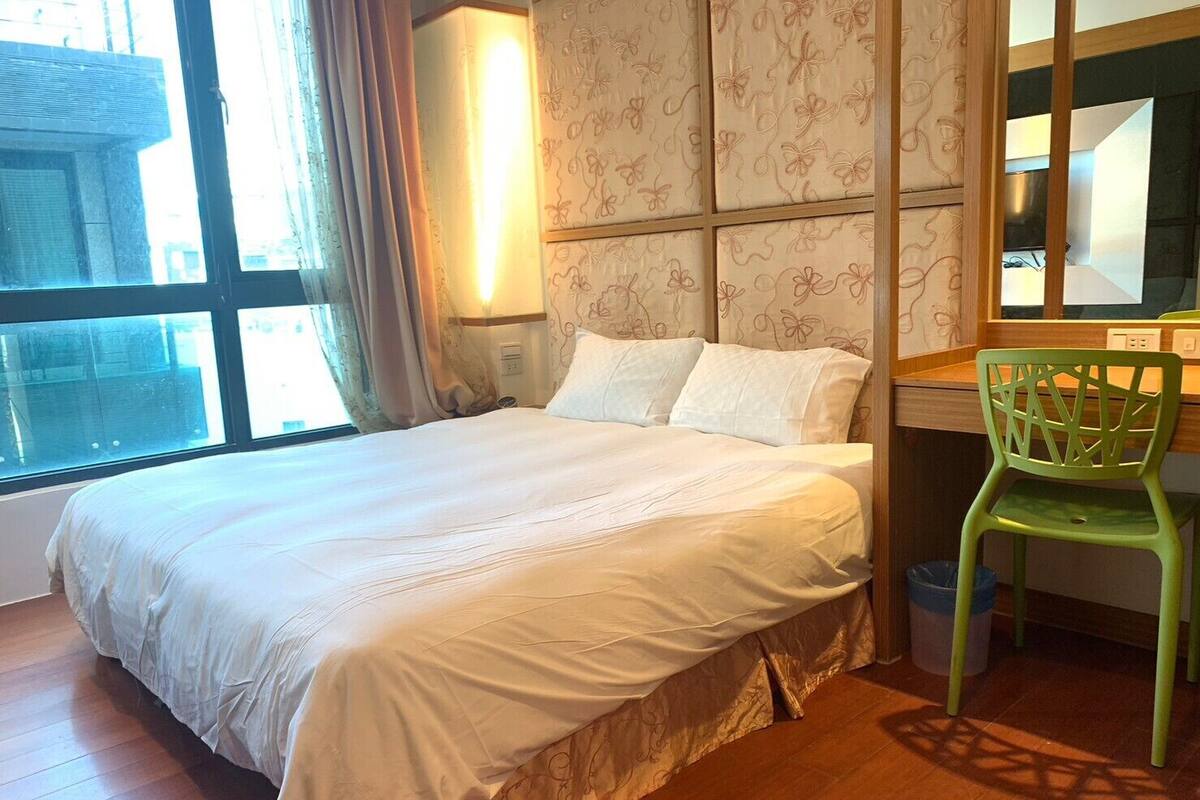 A hotel room with a large bed, a desk, a chair, and a window with curtains.