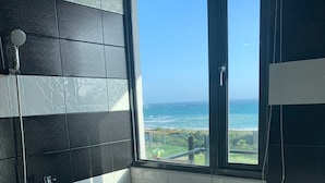 A modern bathroom with a freestanding bathtub, a shower, and a large window offering a view of the ocean. - Happiness Inn (Hengchun)